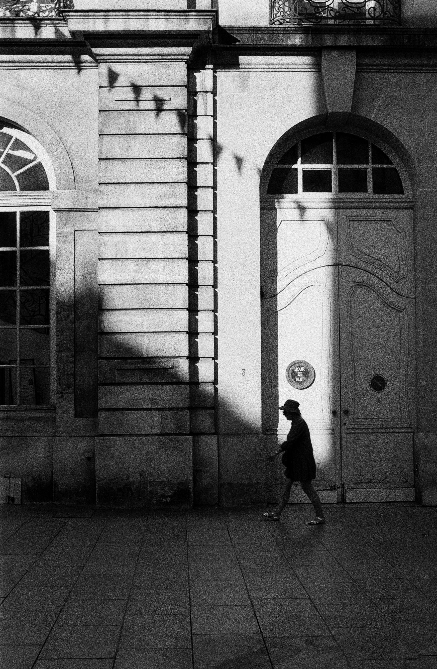Silhouette of a person walking by a historic building in Nancy, France, in black and white.