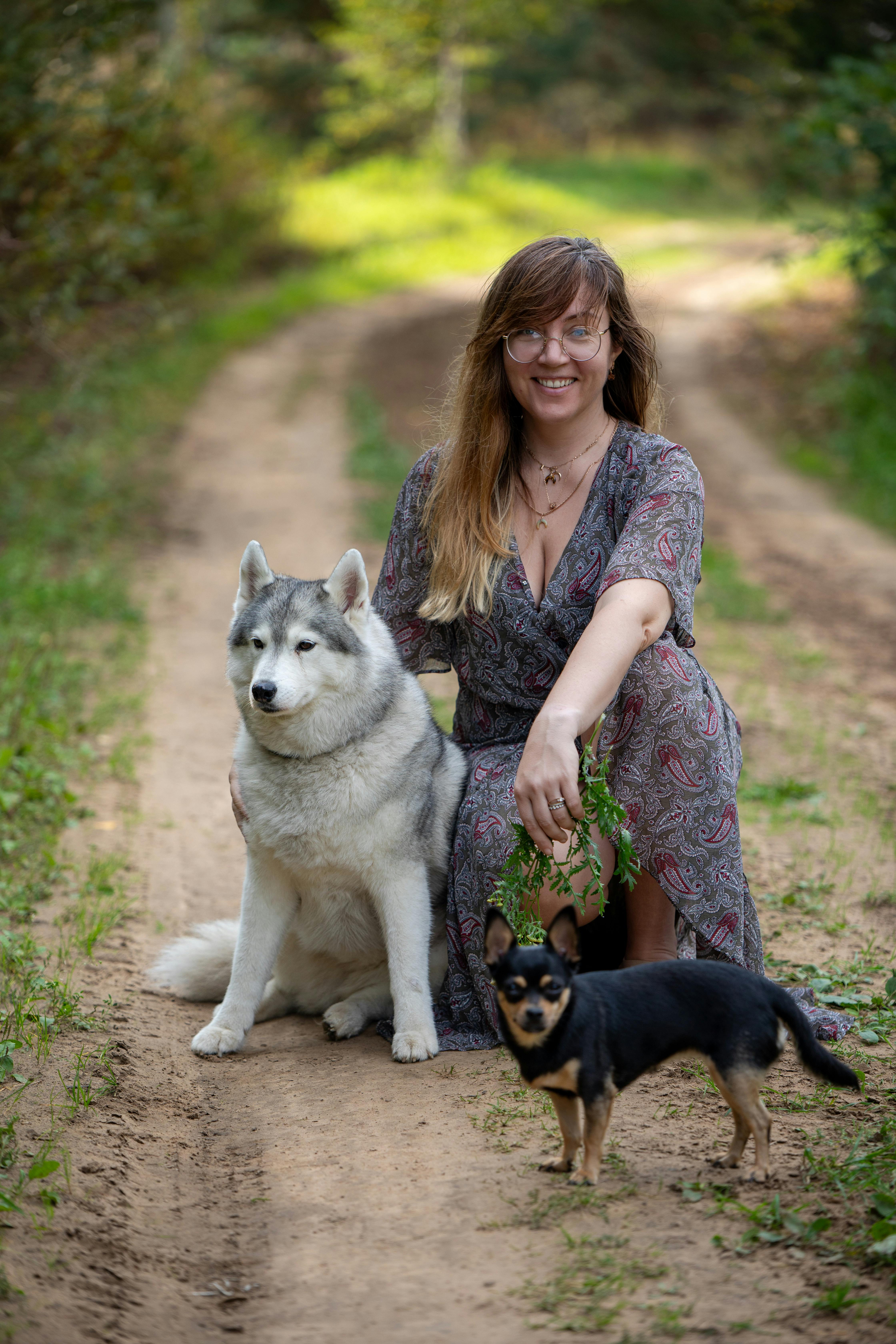 A woman sits with two dogs on a forest path, capturing a serene outdoor moment.