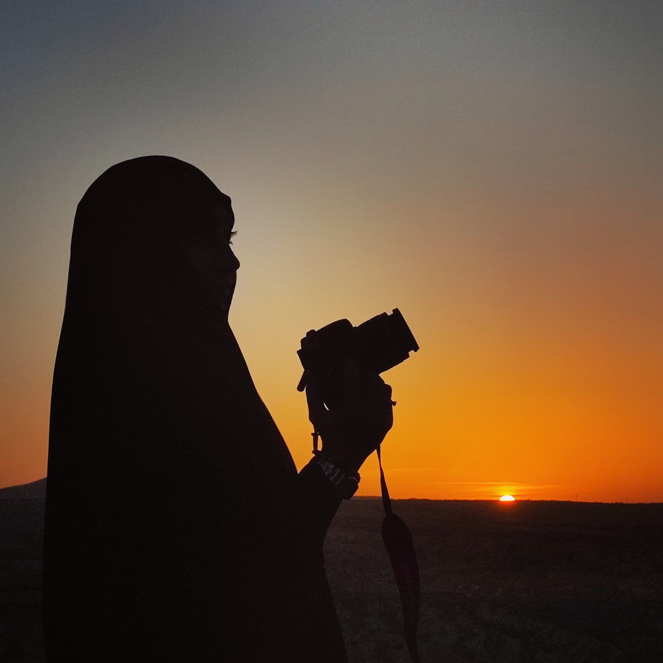 A woman in a hijab holding a camera at sunset · Free Stock Photo