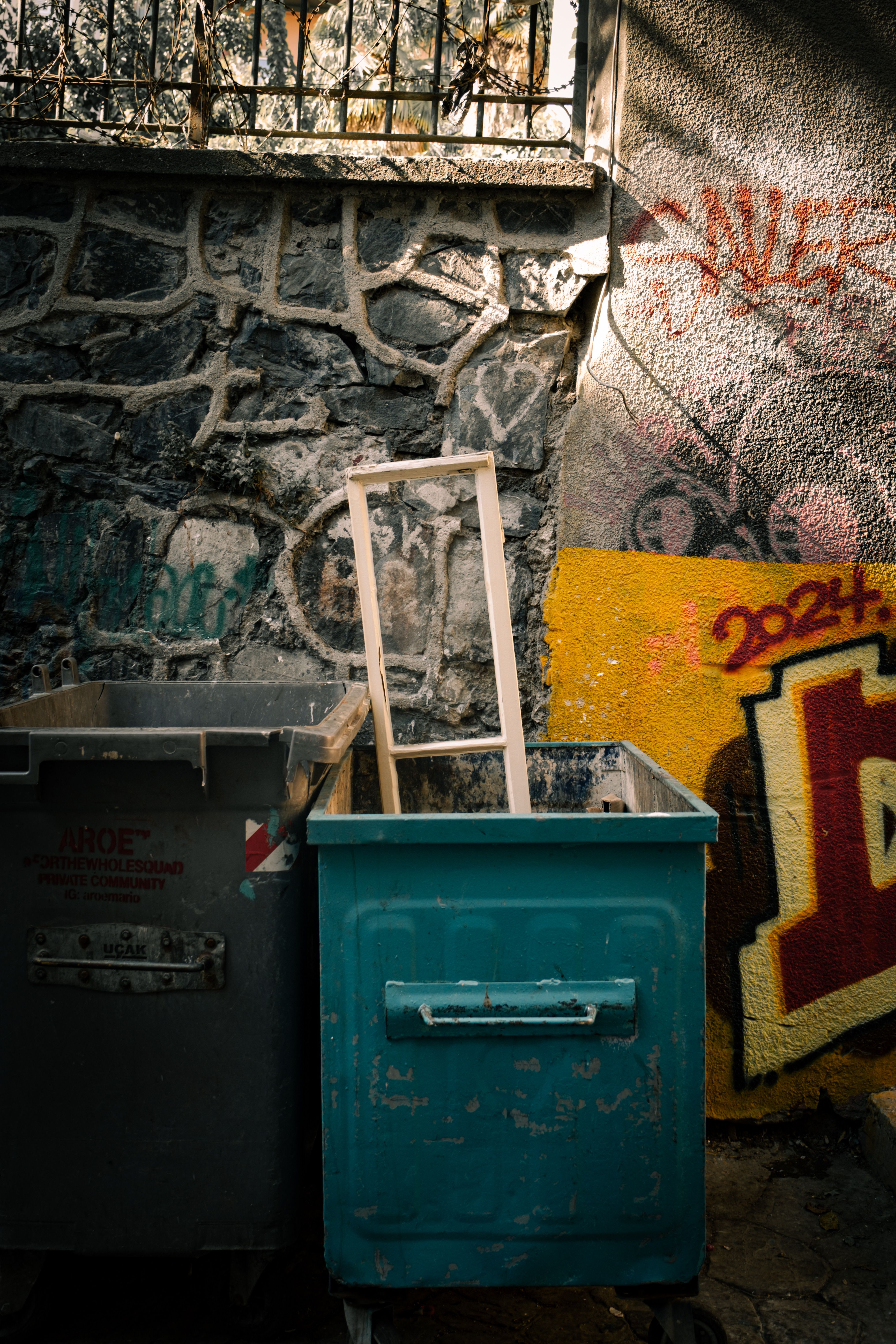 An urban alley with rusty dumpsters, graffiti art, and a stone wall creating a gritty street scene.