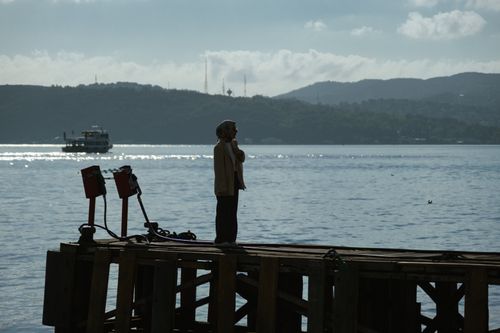 Free A person enjoys a tranquil moment on a pier overlooking the sparkling sea. Stock Photo