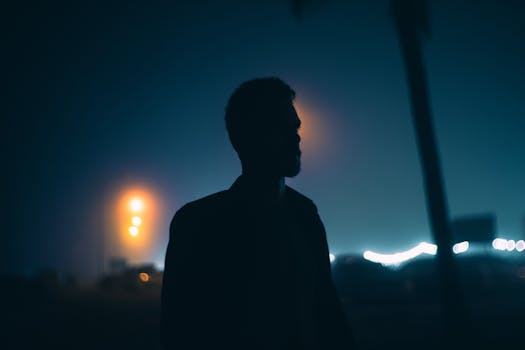 Silhouette of a man outdoors at night in Salalah with a moody teal and orange glow.