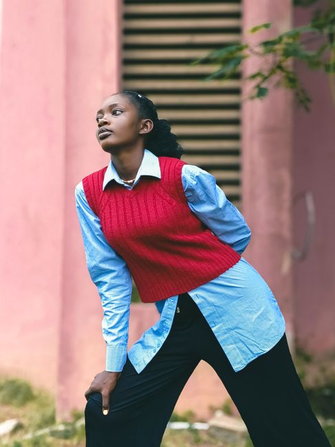 Stylish young woman posing outdoors in a red sweater vest and blue shirt.