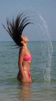 Carefree woman flipping hair in ocean water at sunny beach.