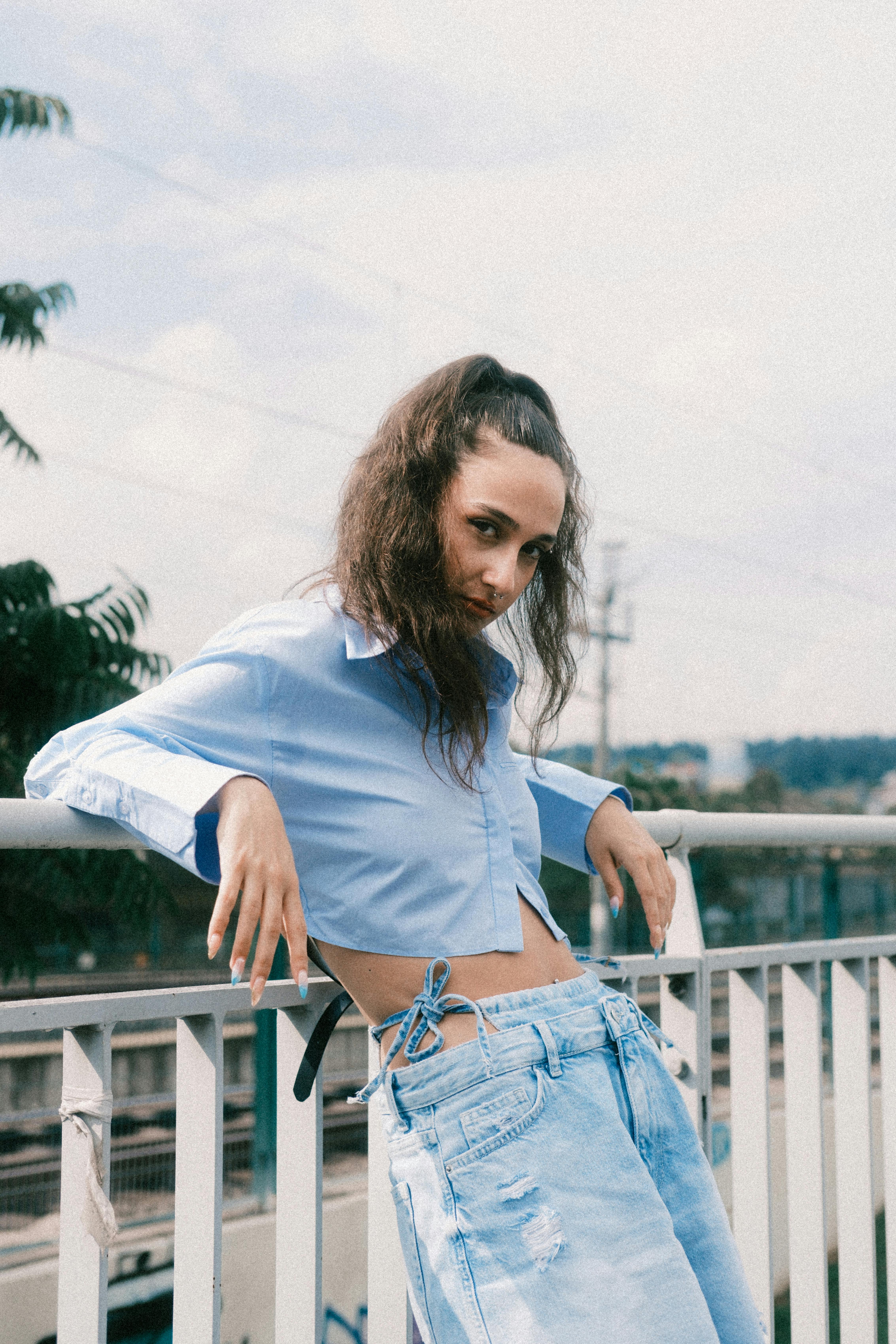 Stylish woman in blue blouse and jeans poses on a sunny day outdoors.
