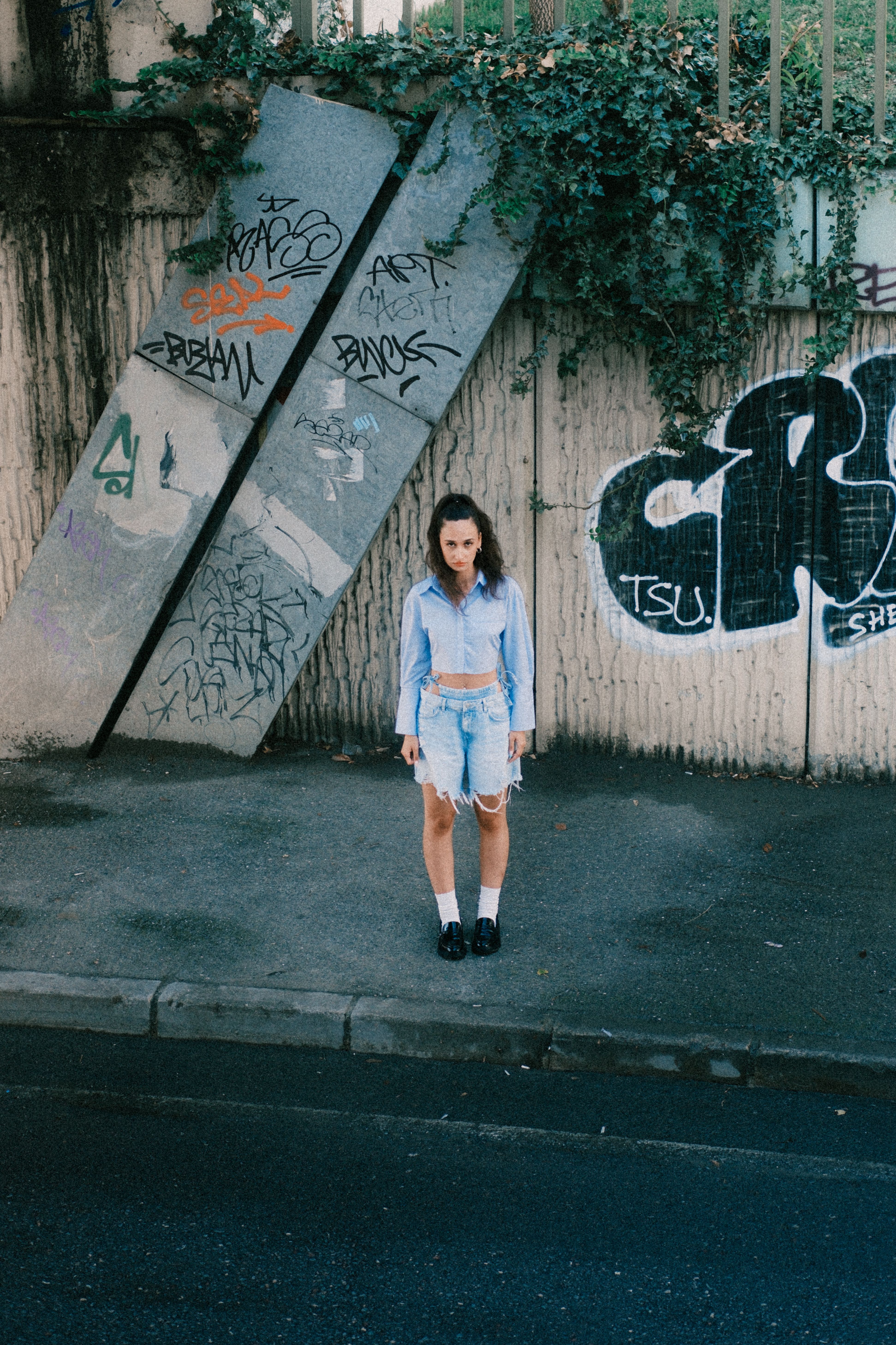 Model in denim outfit poses against graffiti-covered urban backdrop.