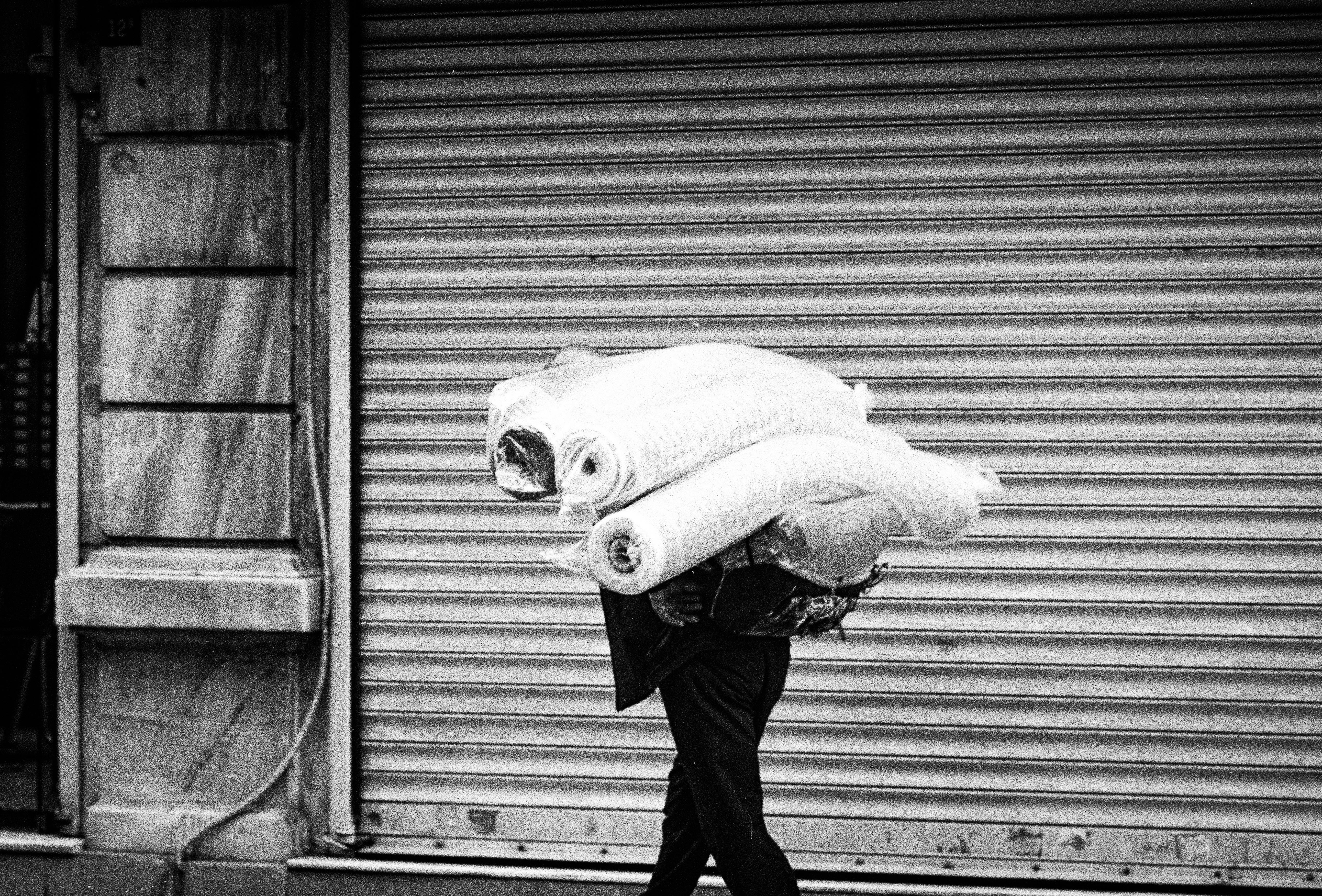 Black and white image of a man carrying rolls of fabric in Istanbul, Türkiye.