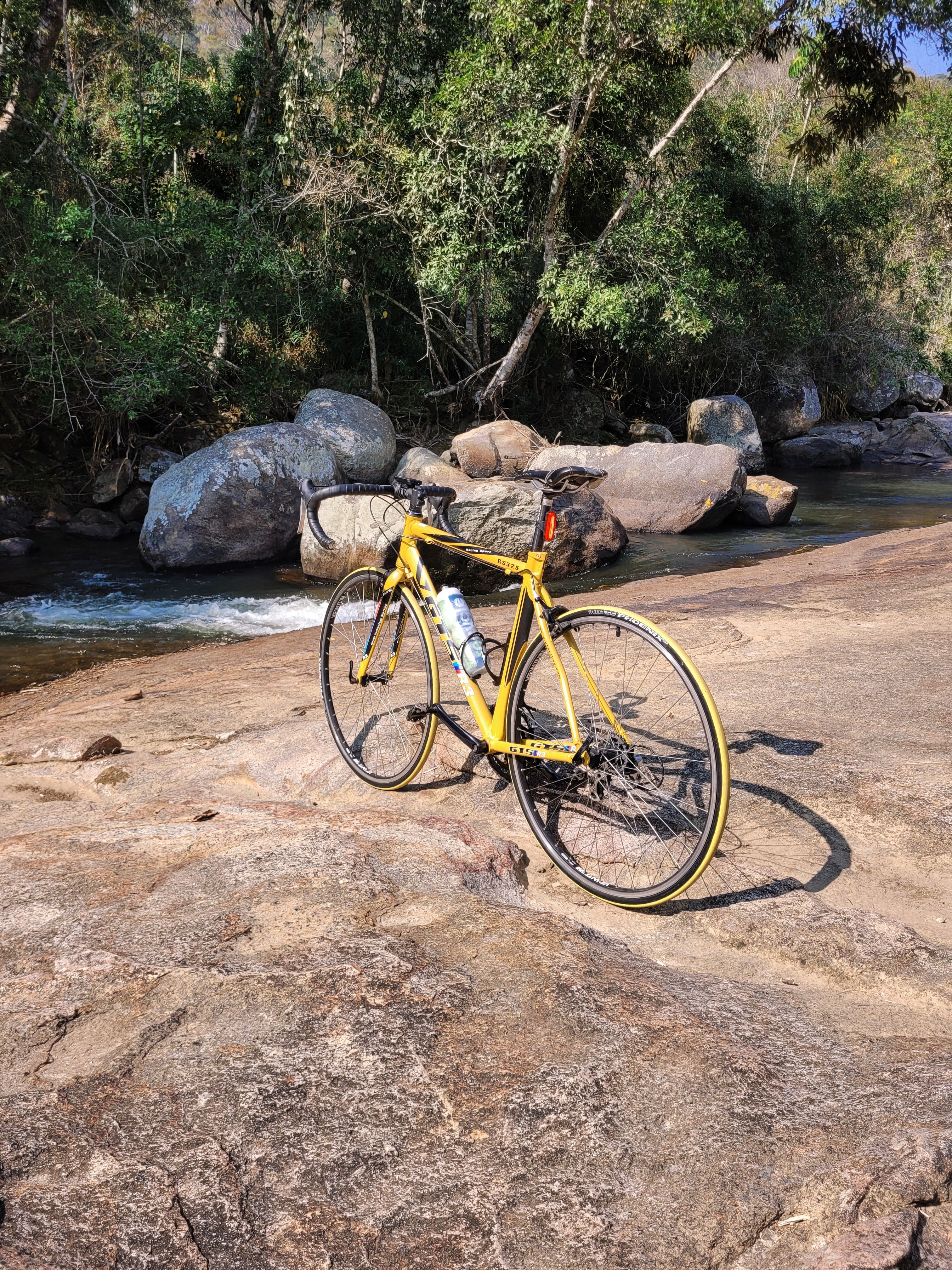A yellow bicycle parked on a rock by a river · Free Stock Photo