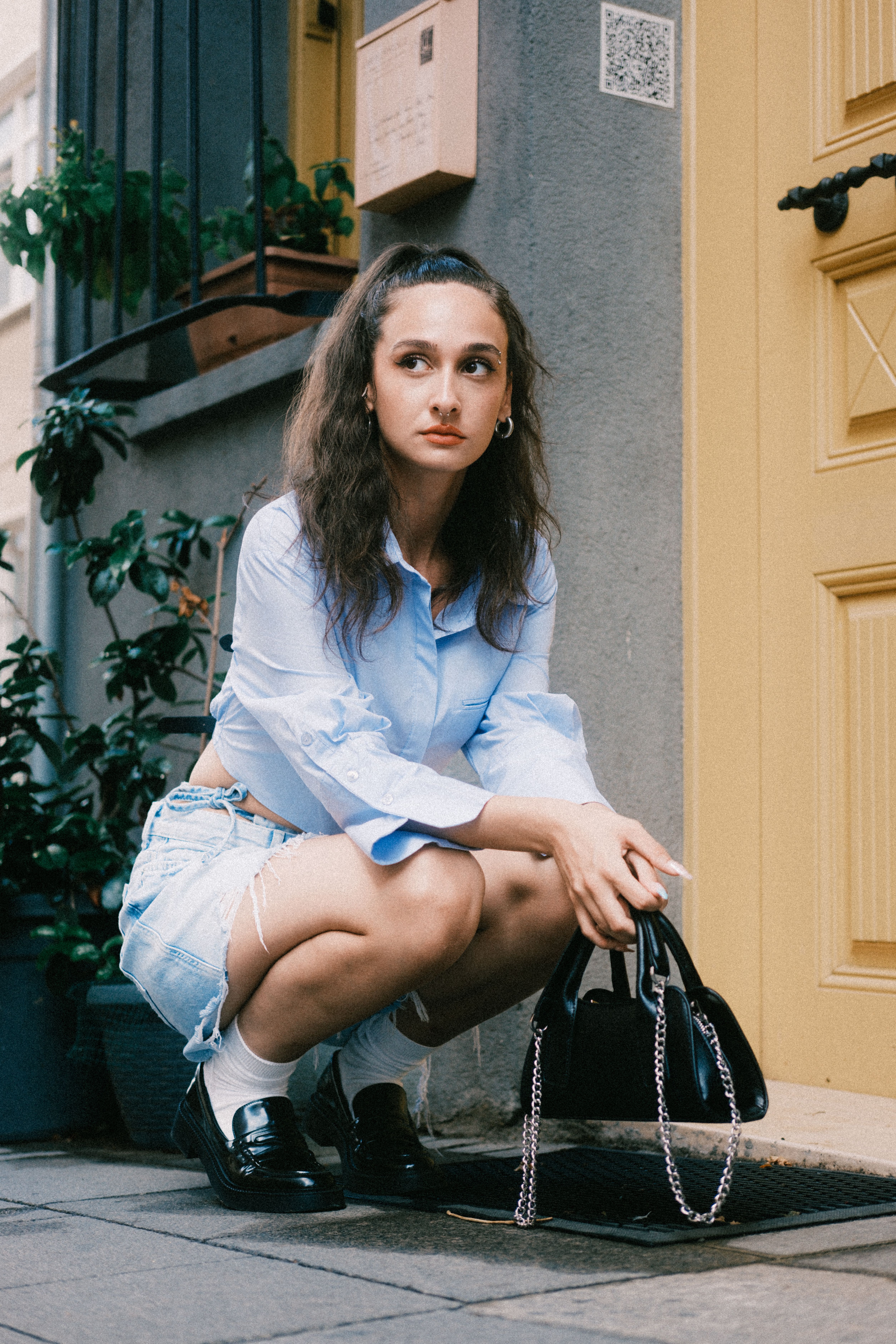 Young woman crouching in fashionable attire on a city street, exuding urban style.