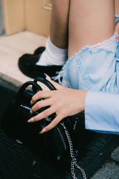 Woman sits outdoors with a stylish black handbag, emphasizing casual elegance.