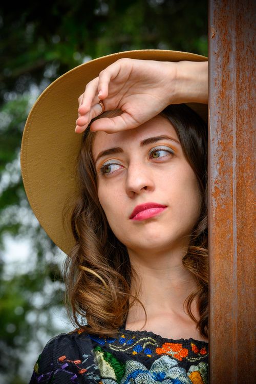 Free A contemplative woman in a sun hat leans against a wooden beam outdoors. Stock Photo