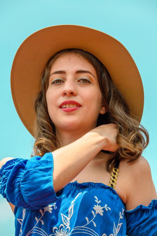 Free A smiling woman in a blue dress and hat poses outdoors under a clear sky. Stock Photo