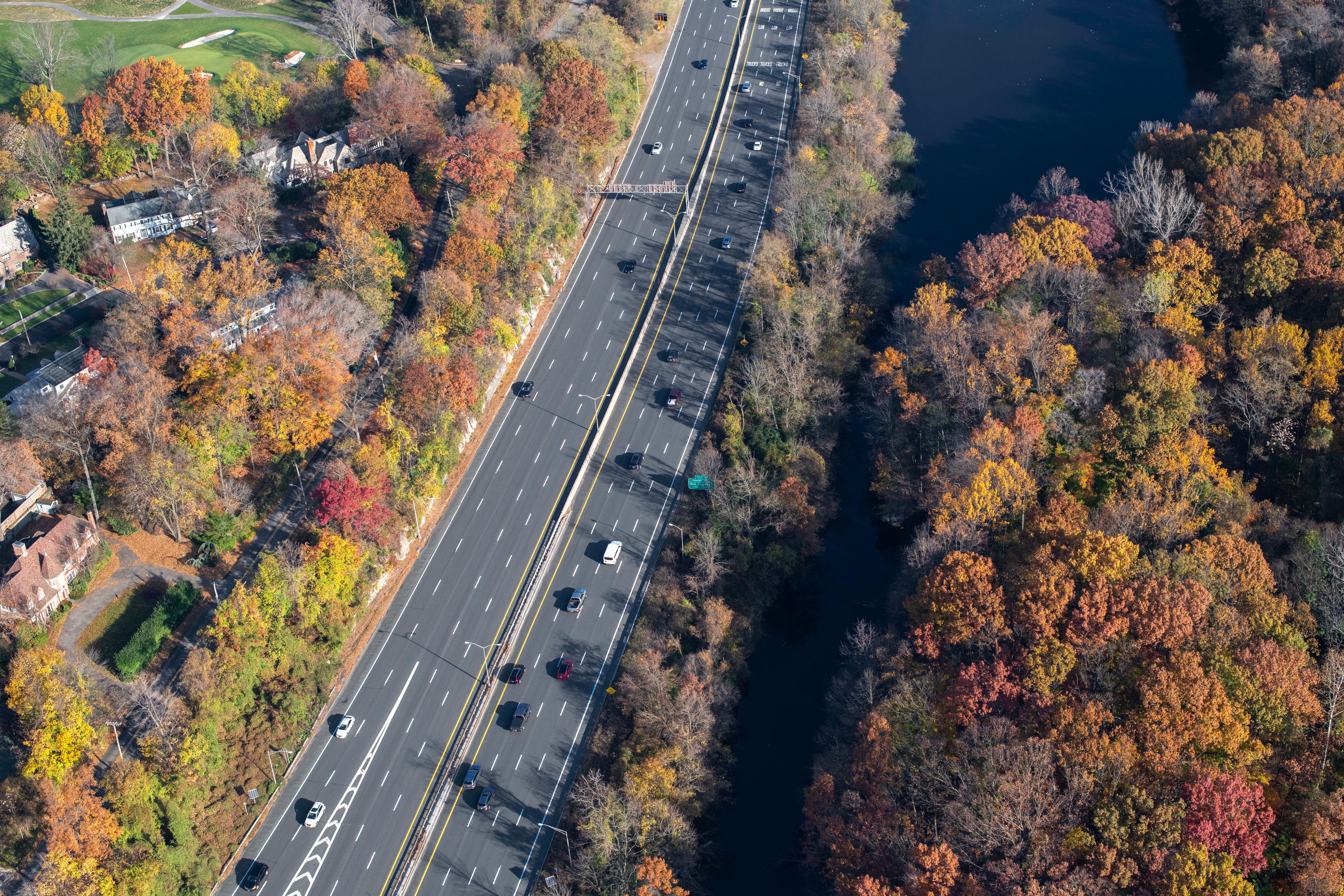 Aerial photo of a highway surrounded by vibrant autumn forests and river.