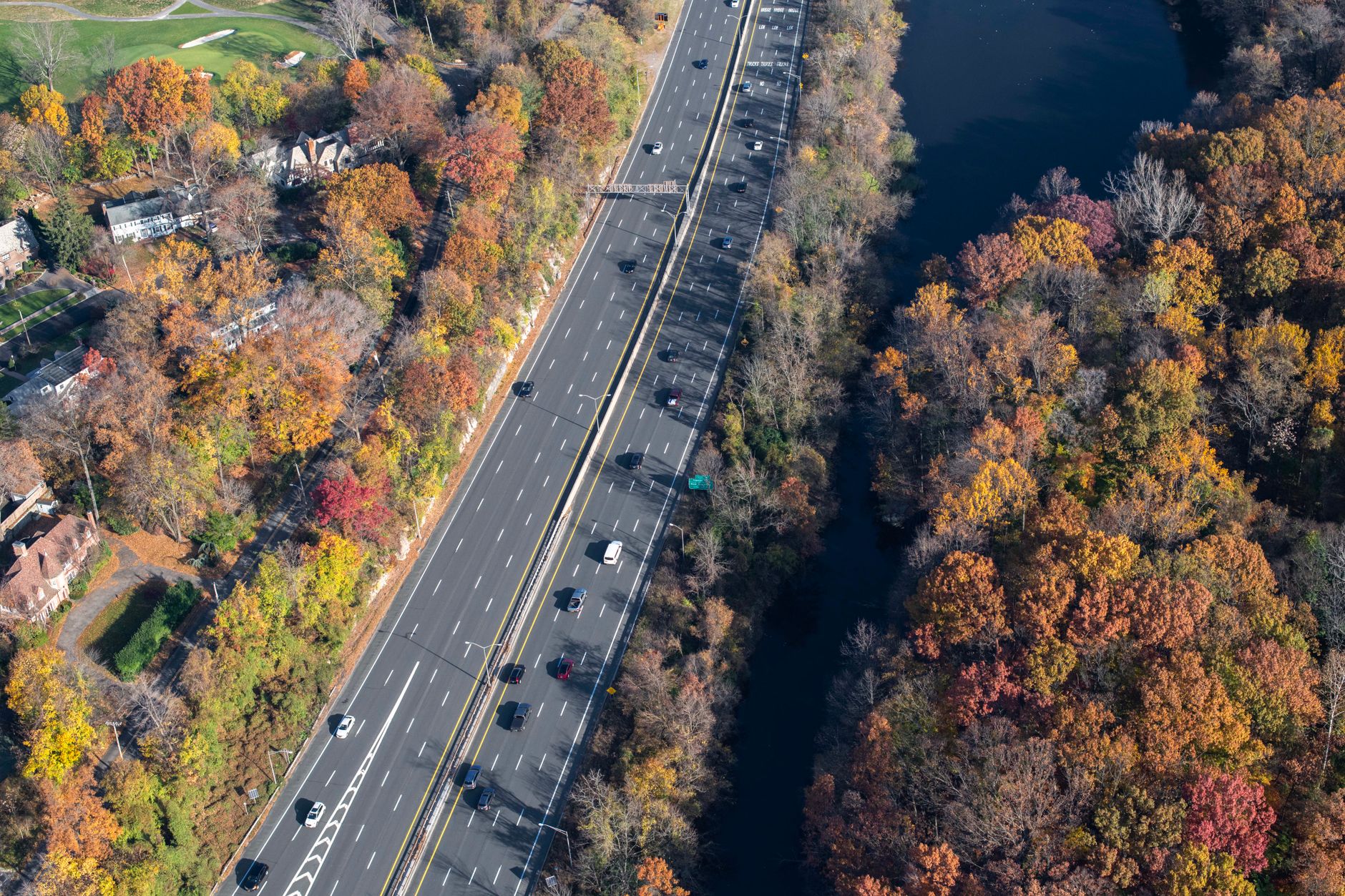 Aerial photo of a highway surrounded by vibrant autumn forests and river.