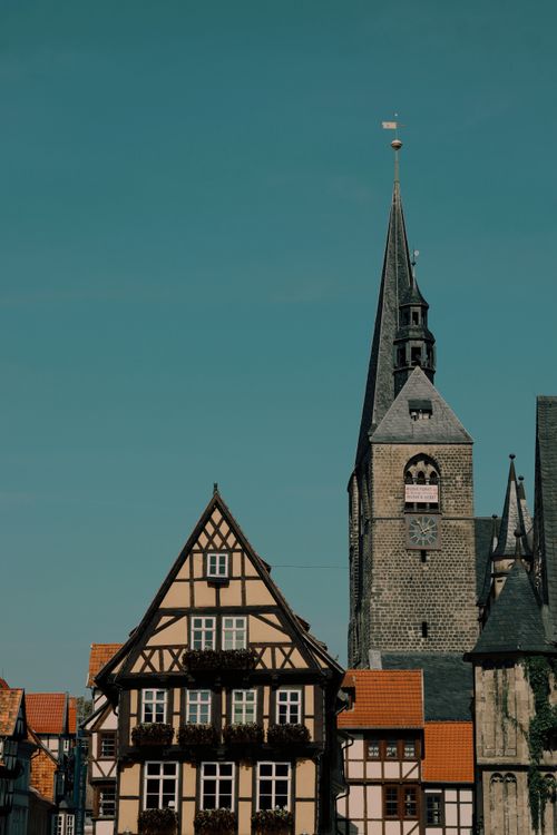 Free Charming Quedlinburg scene with a historic church tower and traditional timber-framed house under the blue sky. Stock Photo