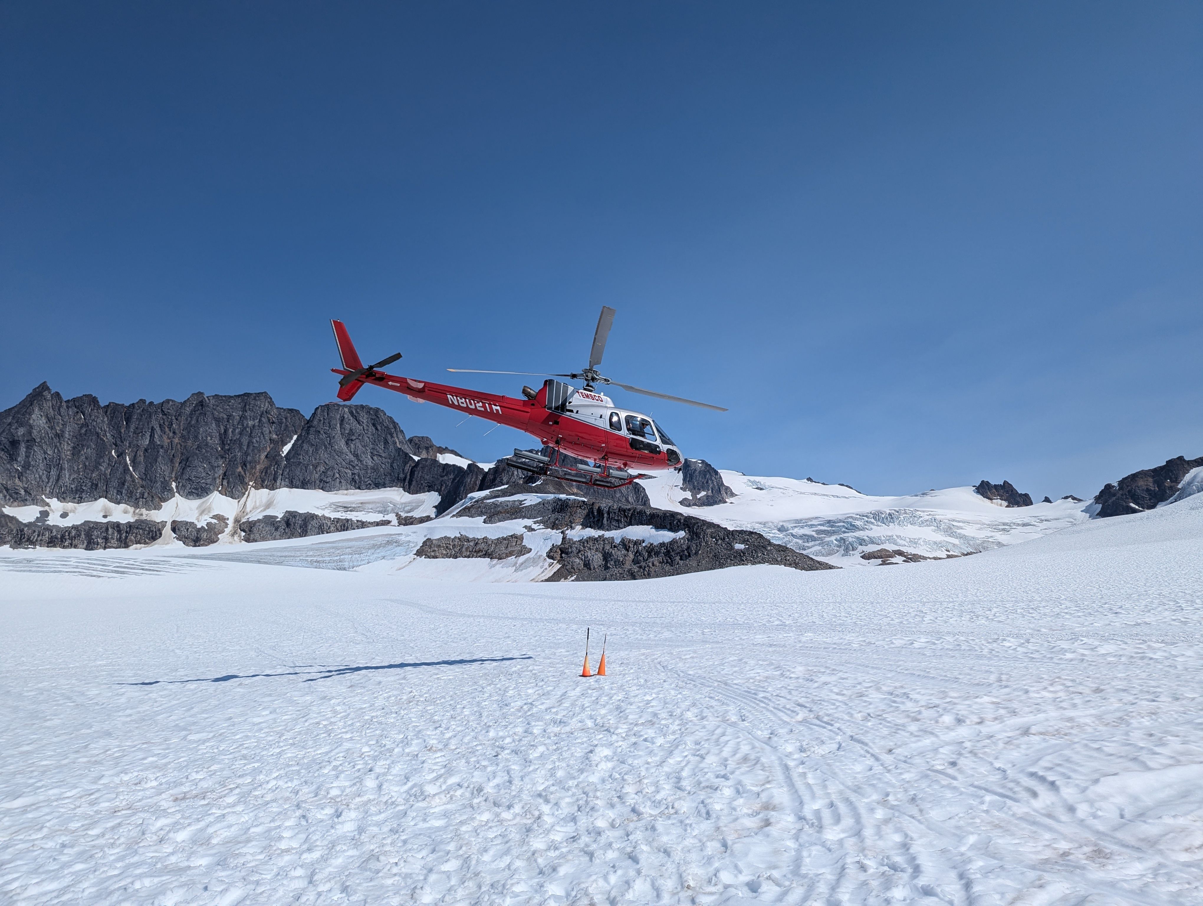Bear Glacier 30 Minute Helicopter Scenic Flight - A red helicopter flies over a snowy glacier landscape in Skagway, Alaska.