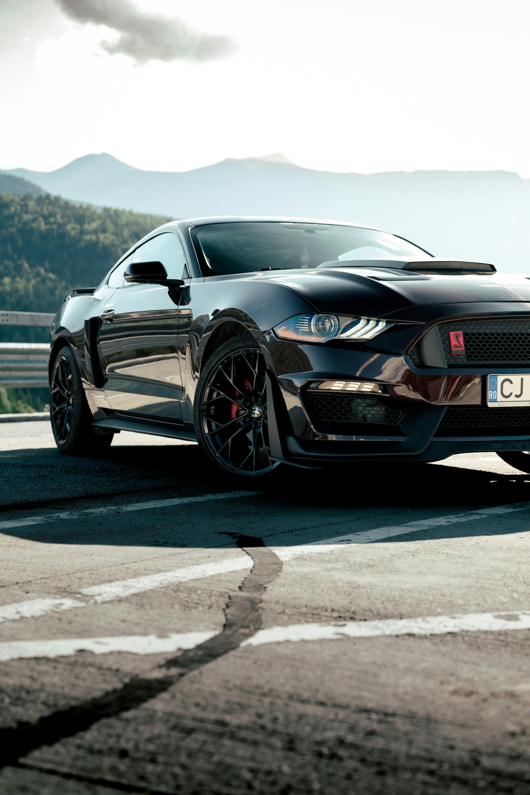 A powerful black Mustang parked on a mountain road, showcasing its sleek design under the sun.