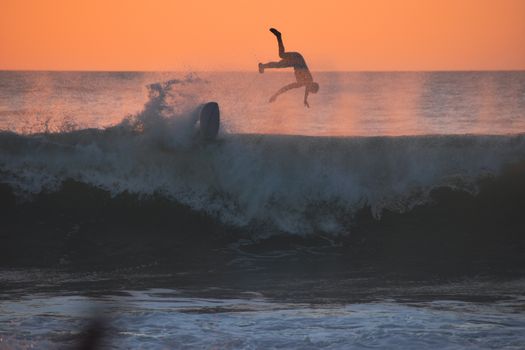 Surfer falls off board amid crashing waves during sunset, highlighting the excitement of water sports.