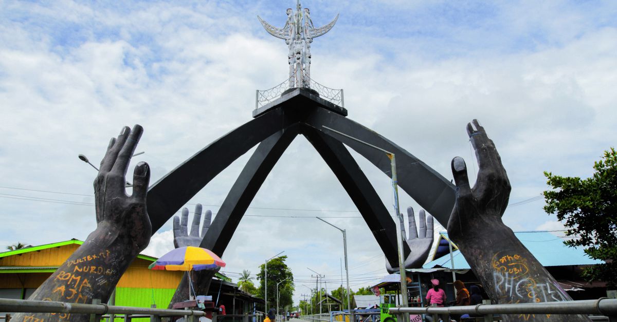 Monument in Agats, Papua with large hands sculpture and urban surroundings.