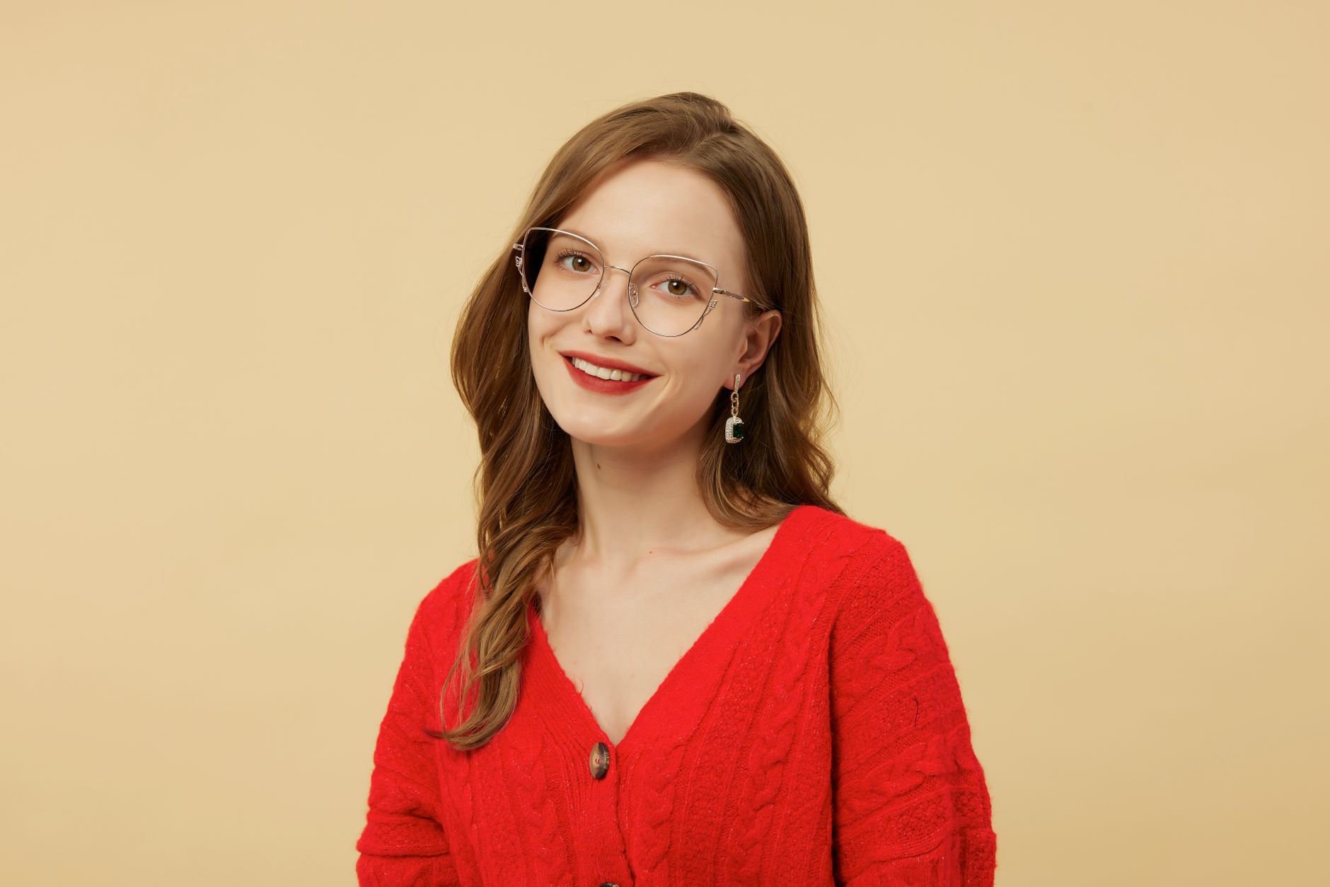 Stylish woman in red sweater and glasses smiling against a neutral background.