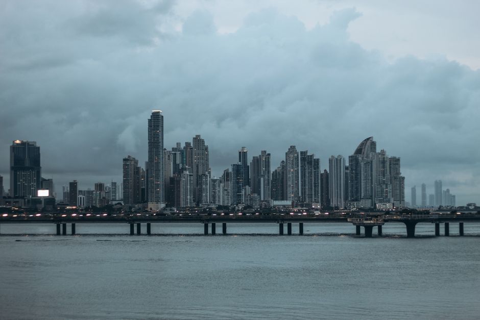Panama City skyline with its iconic skyscrapers under a dramatic cloudy sky at dusk, reflecting on the water.