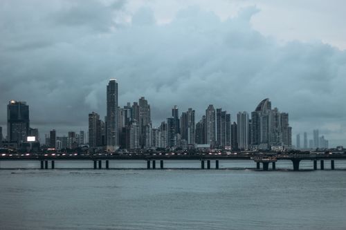 Free Panama City skyline with its iconic skyscrapers under a dramatic cloudy sky at dusk, reflecting on the water. Stock Photo