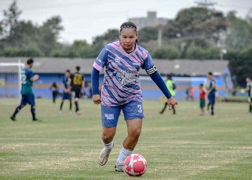 Female soccer player dribbling the ball on a football field during a match.