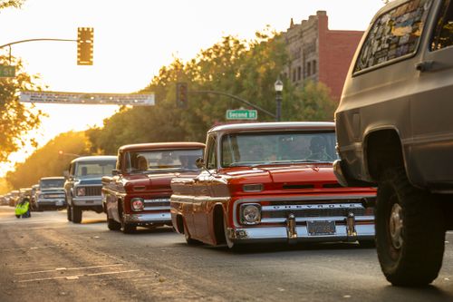 Free Vintage Chevrolet trucks cruising down a sunlit city street during a retro car show. Stock Photo
