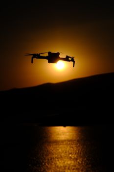 Captivating silhouette of a drone flying against the vibrant backdrop of a sunset over water.