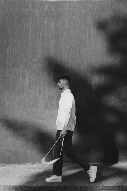 Black and white photo of a man walking on city streets, casting a shadow.