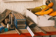 A collection of carpentry tools and safety gear on a dusty workbench in a workshop setting.