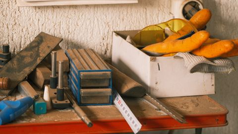 A collection of carpentry tools and safety gear on a dusty workbench in a workshop setting.