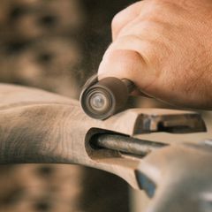 A rotary tool sanding drum shaping a curved piece of wood in a vice