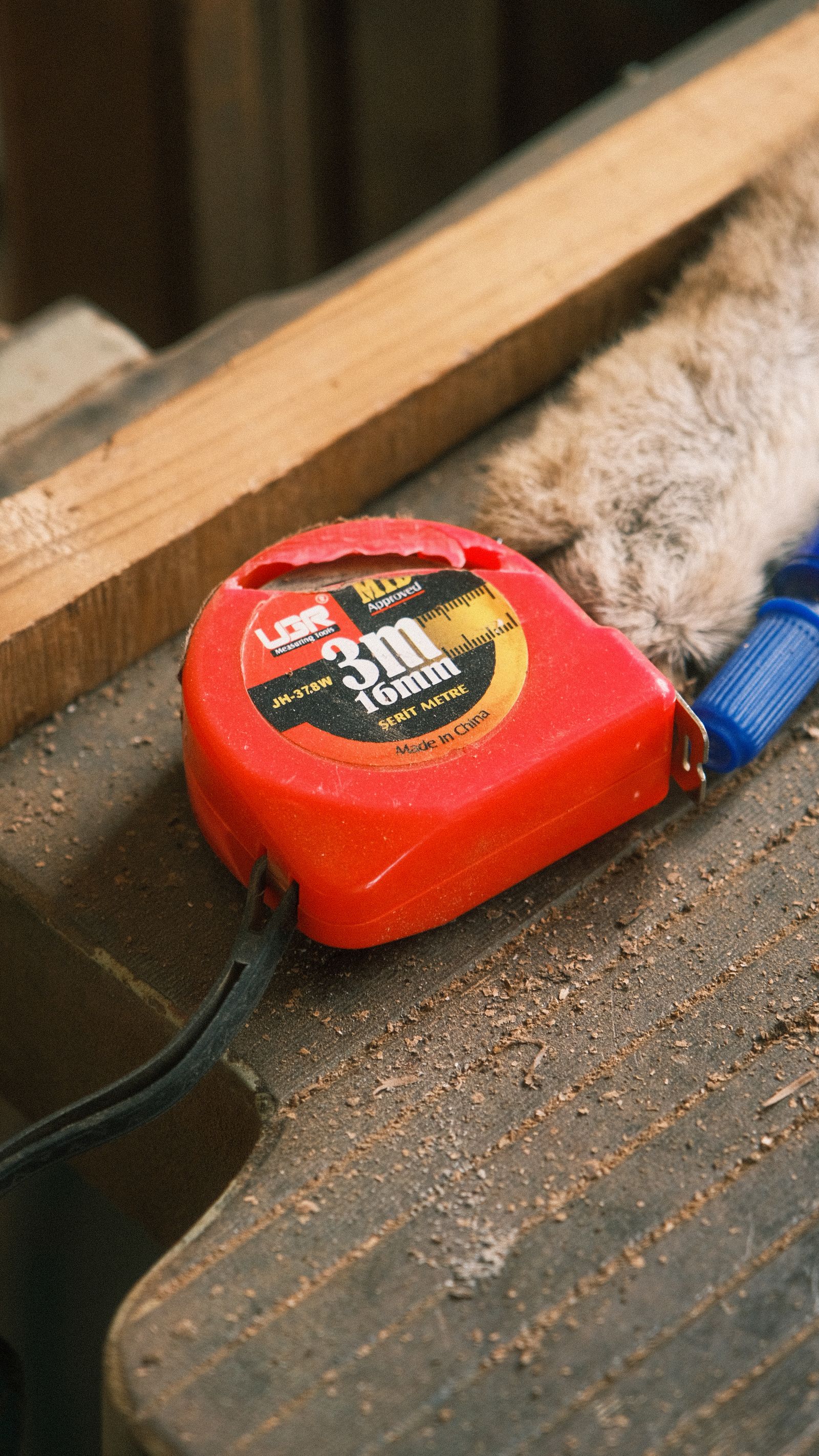 Red tape measure resting on a dusty woodworking bench beside timber
