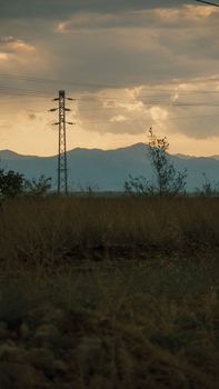 Silhouette of an electric tower in a vast grassland under a sunset sky, symbolizing energy and nature.