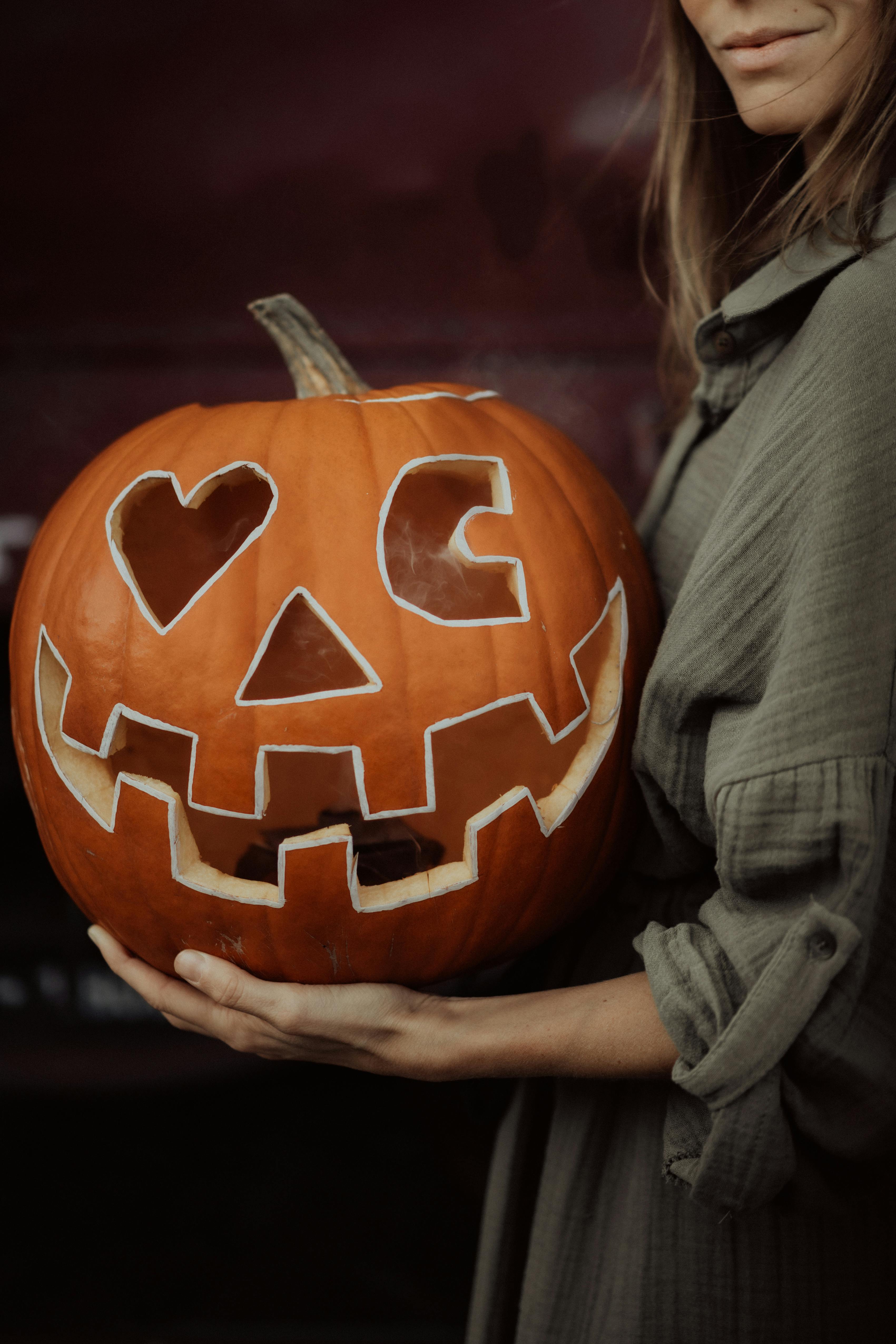 An adult woman holding a carved pumpkin with a spooky face, perfect for Halloween.