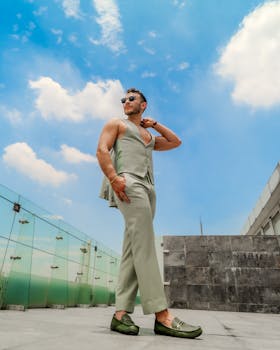 Stylish man posing on a rooftop in Mexico City wearing light attire and sunglasses.