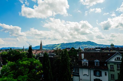 Free A picturesque view of Bern cityscape with a church spire and lush green hills under a cloudy sky. Stock Photo