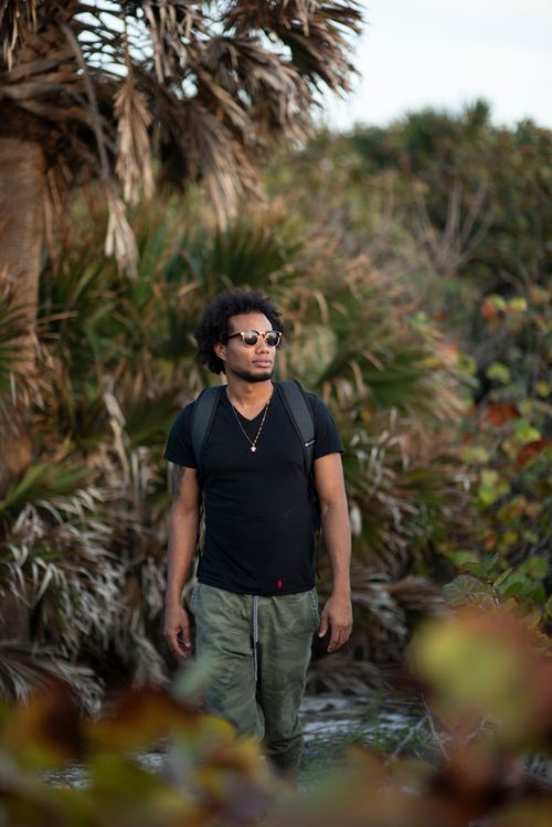 Free A fashionable man enjoys a summer hike through lush greenery, showcasing outdoor leisure and travel. Stock Photo