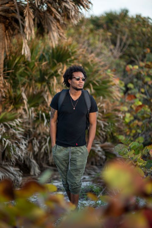 Free A stylish man walks through a vibrant forest wearing casual attire, showcasing summer adventure fashion. Stock Photo