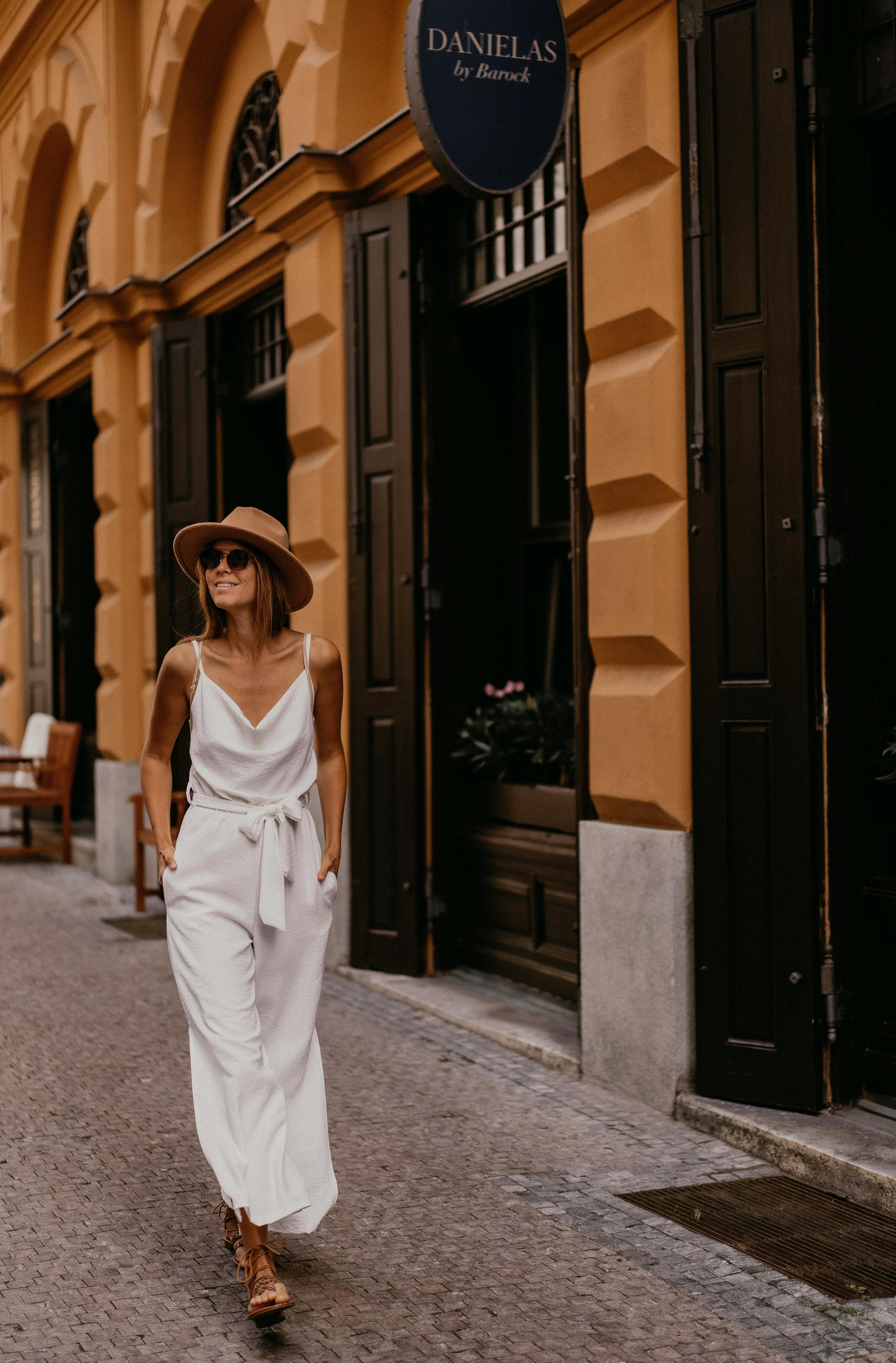 Stylish woman in white outfit and hat walking down a charming street in Prague's historic district.