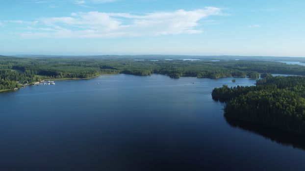 Stunning aerial view of a vast Finnish lake surrounded by lush forests under a clear blue sky.