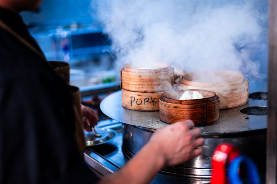 Chef preparing fresh pork dumplings in bamboo steamers, kitchen setting.