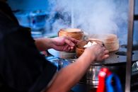 Chef preparing steaming dim sum baskets in a professional kitchen.