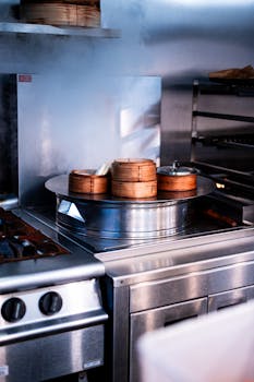 Close-up of steaming bamboo baskets on a stainless steel stove in a restaurant kitchen.
