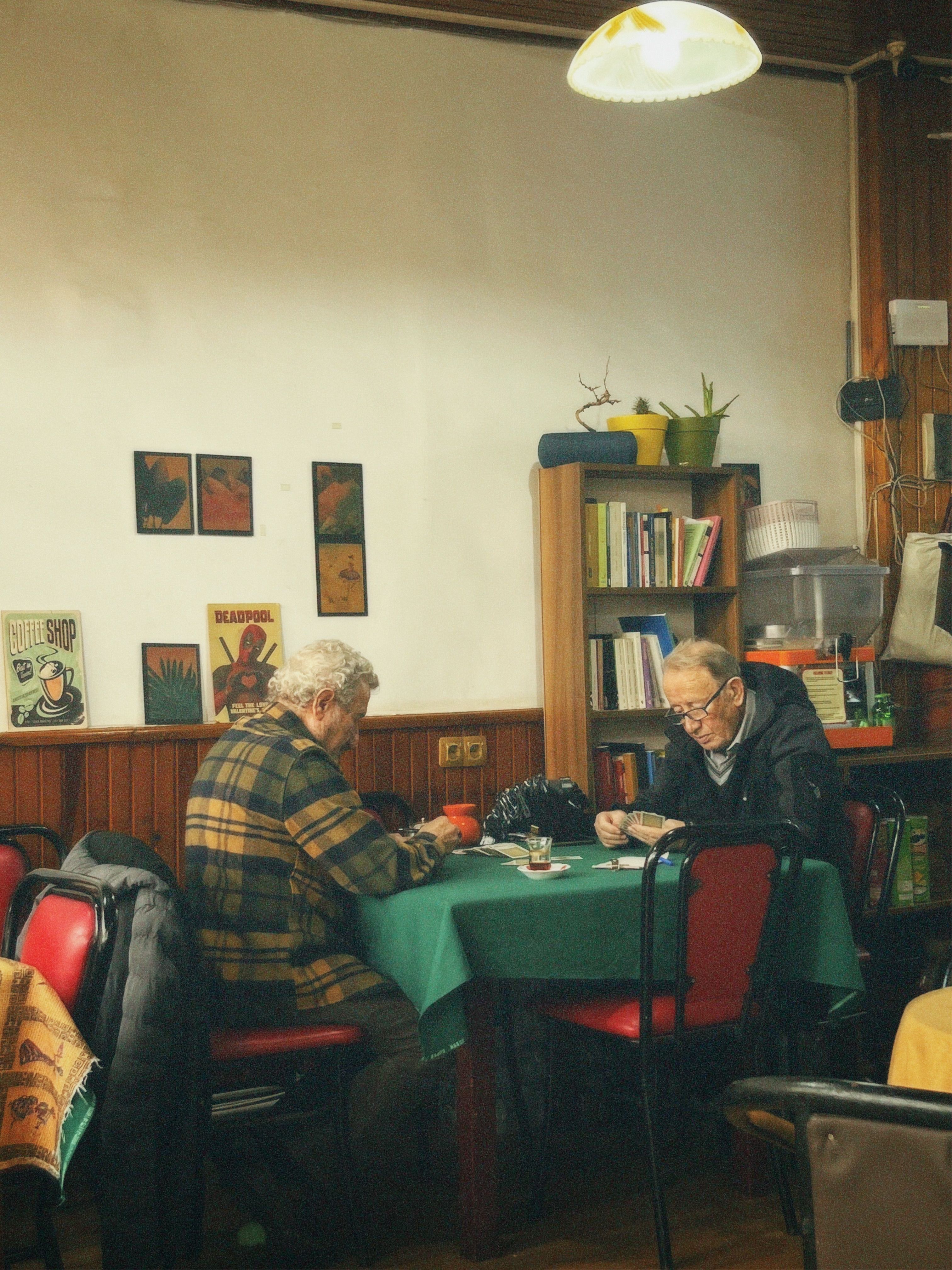 Two senior men playing cards in a cozy room with vintage decor and warm lighting.