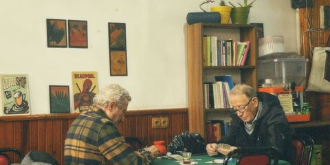 Two senior men playing cards in a cozy room with vintage decor and warm lighting.