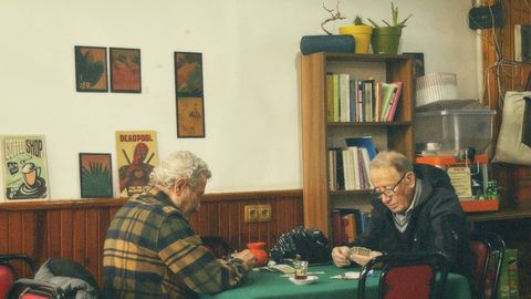Two senior men playing cards in a cozy room with vintage decor and warm lighting.