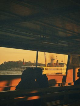 A scenic view of a city and watercraft captured from a ferry during sunset, highlighting reflections and silhouettes.