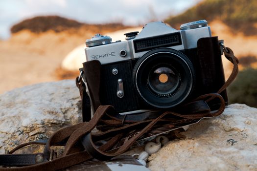 Capture nostalgia with this vintage Zenit-E camera on a sunlit beach rock.